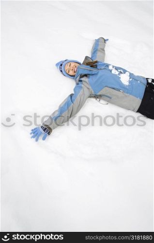 Attractive smiling mid adult Caucasian woman wearing blue ski clothing lying in snow with eyes closed making snow angel.