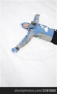 Attractive smiling mid adult Caucasian woman wearing blue ski clothing lying in snow with eyes closed making snow angel.