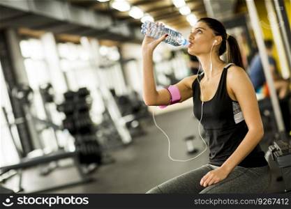 Attractive sport young woman drinking water while sitting and resting after workout