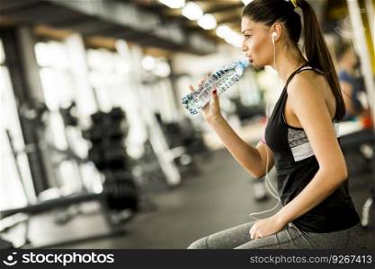 Attractive sport young woman drinking water while sitting and resting after workout