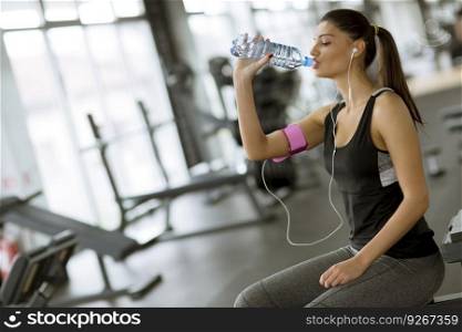 Attractive sport young woman drinking water while sitting and resting after workout in the gym