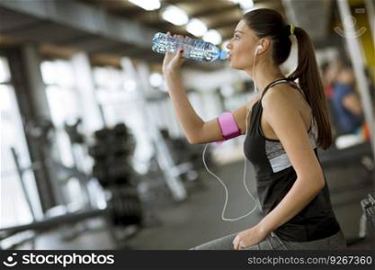 Attractive sport young woman drinking water while sitting and resting after workout in the gym