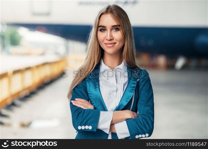 Attractive stewardess in uniform poses against airport building. Air hostess in suit near terminal. Flight attendant occupation. Stewardess in uniform against airport building