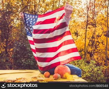Attractive, stylish man holding a waving US Flag on the background of the rays of the setting sun and yellow trees. View from the back. Preparing for the holidays. Attractive, stylish man holding a waving US Flag