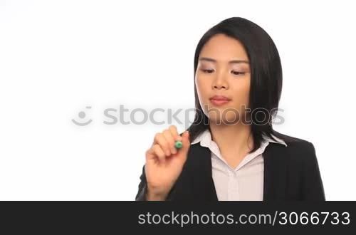 Attractive stylish young Asian businesswoman writing on a virtual screen interface with a pen against a white studio background