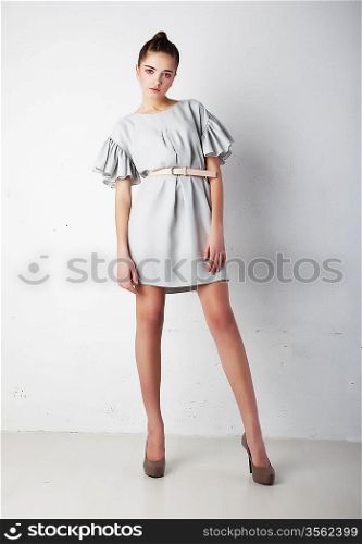 Attractive stylish young brunette female fashion model posing over white wall