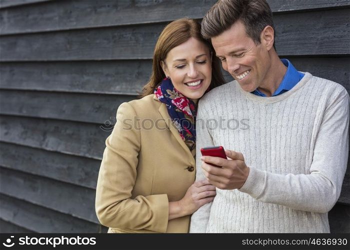 Attractive, successful and happy middle aged man and woman couple together outside using mobile cell phone