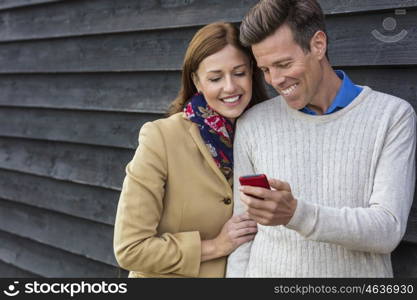 Attractive, successful and happy middle aged man and woman couple together outside using mobile cell phone