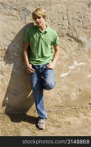 Attractive teen boy leaning against wall in sunlight.