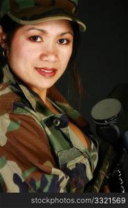 Attractive thirty something Filipino woman in camo fatigues with paintball rifle.