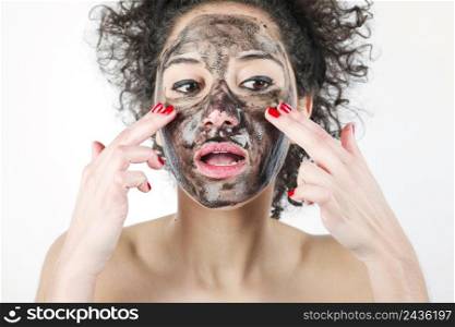 attractive woman applying black face mask with her fingers against white background