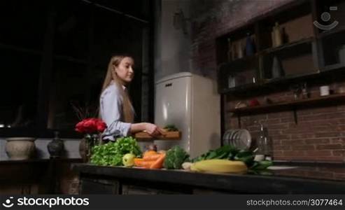 Attractive woman bringing wooden tray with ingredients for vegetarian smoothie and laying out fruits on the table in grunge styled kitchen. Foreground colorful fruits and vegetables on kitchen table. Healthy vegetarian diet for weight loss and detox