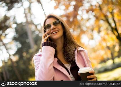 Attractive woman drinking coffee in autumn park and using mobile phone