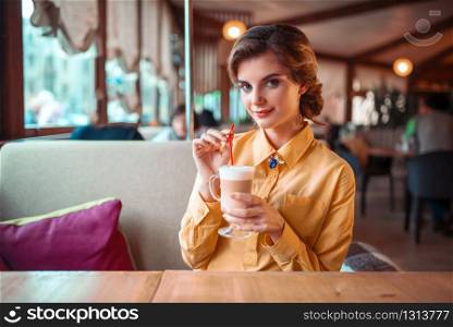 Attractive woman drinks a cocktail from the straw, restaurant on background. Attractive woman drinks a cocktail from the straw