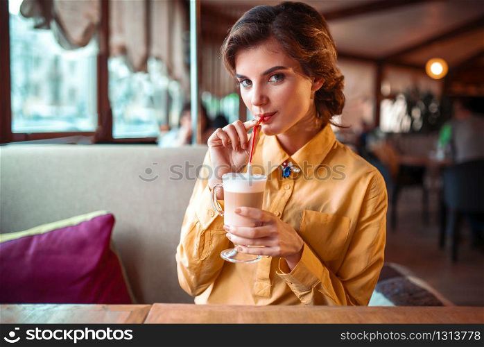 Attractive woman drinks a cocktail from the straw, restaurant on background