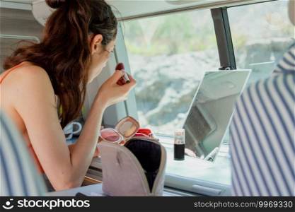 Attractive woman in bikini, looks at herself in a mirror while making up inside her c&er van, road trip concept