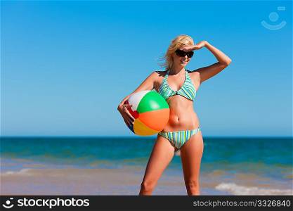 Attractive Woman in bikini standing in the sun on beach under a blue sky - she is covering her eyes with her hand