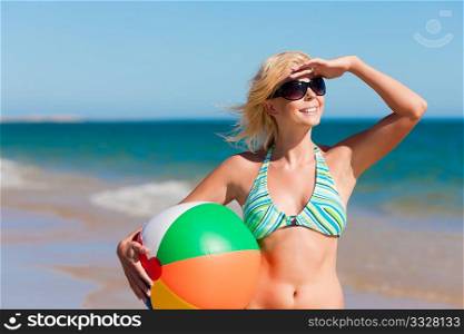 Attractive Woman in bikini standing in the sun on beach under a blue sky ? she is looking into the sky