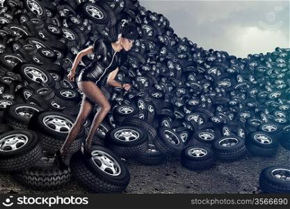 Attractive woman in dress running on tires on cloudy sky