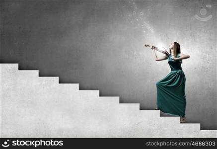 Attractive woman in long green dress playing violin. Elegant violinist player