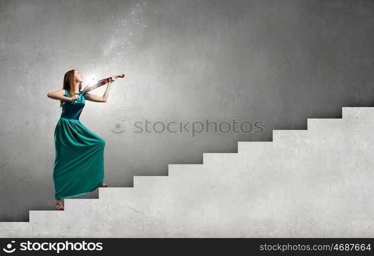 Attractive woman in long green dress playing violin. Elegant violinist player