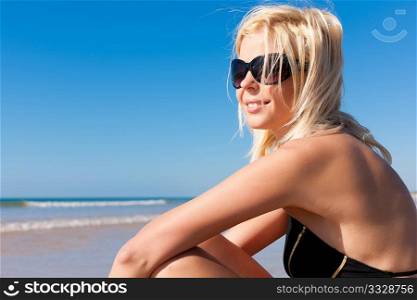 Attractive Woman in monokini sitting in the sun on beach, a lot of copyspace in the blue sky