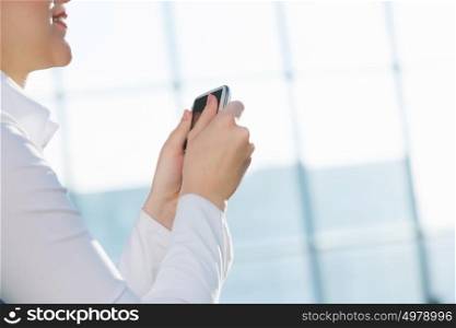 Attractive woman in office building. Hands of woman in modern glass interior using her smartphone