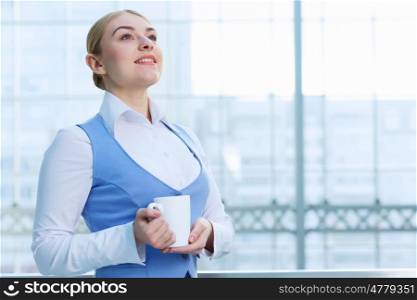 Attractive woman in office building. Young blond woman in modern glass interior with mug in hands