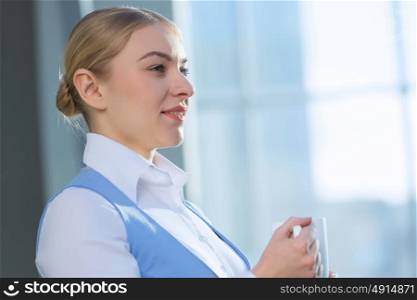Attractive woman in office building. Young blond woman in modern glass interior with mug in hands