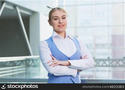 Attractive woman in office building. Young blond woman in modern glass interior arms crossed on chest