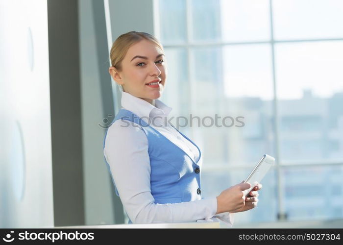 Attractive woman in office building. Young blond woman in modern glass interior using tablet