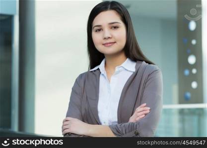 Attractive woman in office building. Young brunette woman in modern glass interior arms crossed on chest