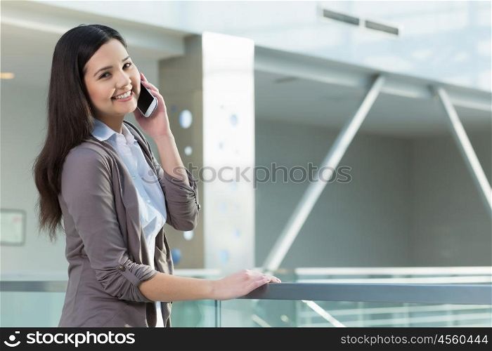 Attractive woman in office building. Young brunette woman in modern glass interior talking on mobile phone