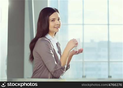 Attractive woman in office building. Young brunette woman in modern glass interior with mug in hands
