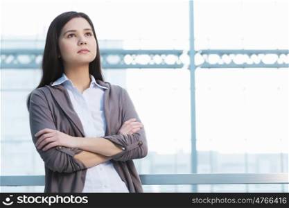 Attractive woman in office building. Young brunette woman in modern glass interior arms crossed on chest
