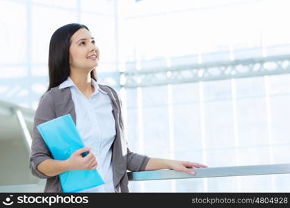 Attractive woman in office building. Young brunette woman in modern glass interior with folder in hands