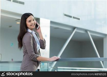 Attractive woman in office building. Young brunette woman in modern glass interior talking on mobile phone