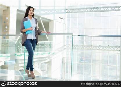 Attractive woman in office building. Young brunette woman in modern glass interior with folder in hands