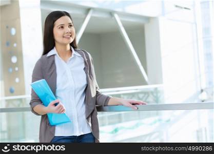 Attractive woman in office building. Young brunette woman in modern glass interior with folder in hands