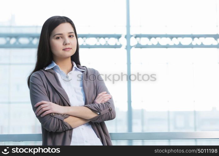 Attractive woman in office building. Young brunette woman in modern glass interior arms crossed on chest