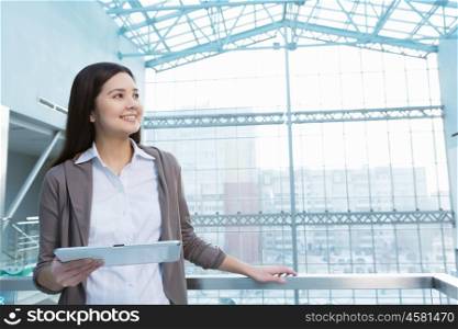 Attractive woman in office building. Young brunette woman in modern glass interior using tablet