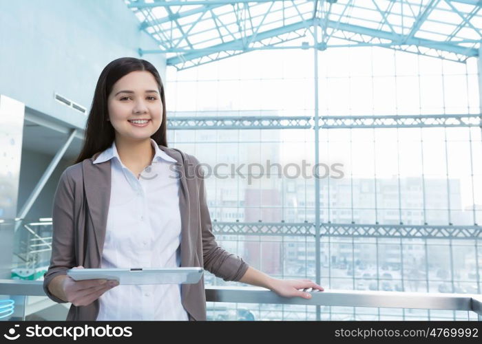 Attractive woman in office building. Young brunette woman in modern glass interior using tablet