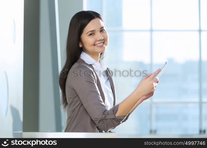 Attractive woman in office building. Young brunette woman in modern glass interior using tablet