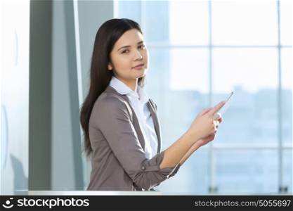 Attractive woman in office building. Young brunette woman in modern glass interior using tablet