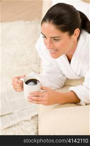 Attractive woman in white bathrobe with coffee newspapers in lounge
