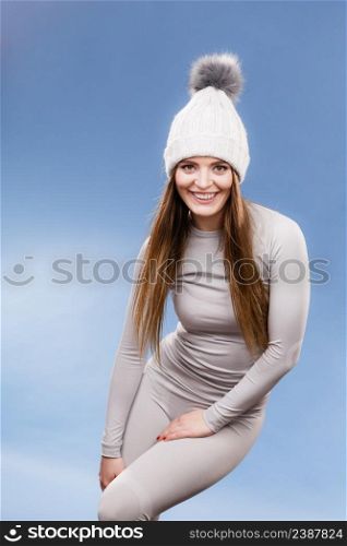 Attractive woman in winter cap and gray sports thermolinen underwear for skiing training studio shot on blue. Long sleeves top and leggings. woman in thermal underwear