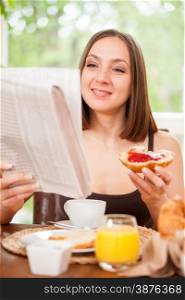 Attractive woman is reading the newspaper while having breakfast at home