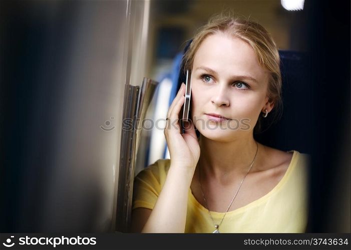 Attractive woman listening to a call on her mobile phone looking into the distance with a thoughtful expression while travelling by train