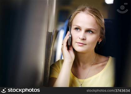 Attractive woman listening to a call on her mobile phone looking into the distance with a thoughtful expression while travelling by train
