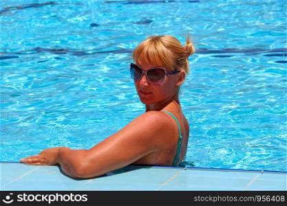 Attractive woman posing during relaxing in swimming pool during vacation. Young woman in sunglasses enjoying summer vacations. Summer holiday in tropical resort. Woman resting in swimming pool. Attractive woman posing during relaxing in swimming pool during vacation